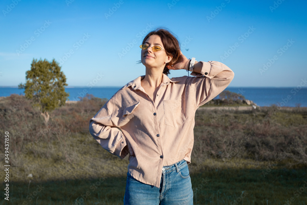 Fashion lifestyle portrait of young trendy woman dressed in shirt and jeans laughing, smiling, posing n the beach