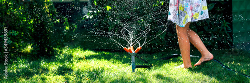 Child playing with garden sprinkler. Happy Girl in dress running and jumping. Kids gardening. Summer outdoor water fun. Children play with gardening hose watering flowers.