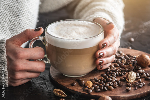 Women s hands in a warm sweater are holding a cup of fragrant latte. The nails are coated with brown nail polish. Coffee manicure. Breakfast or a break in a cozy cafe