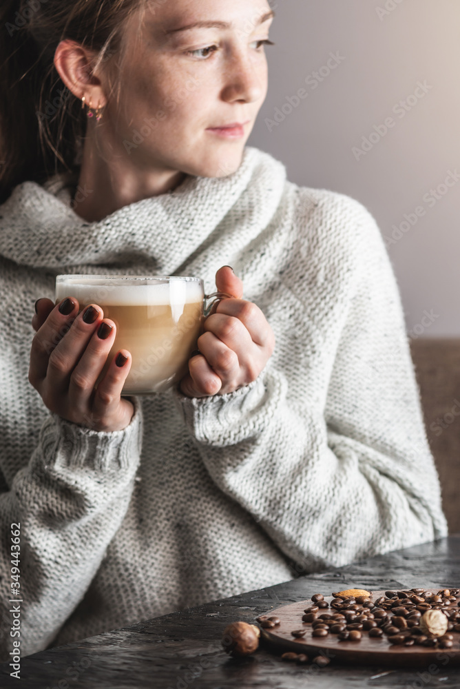 A young beautiful woman in a light warm sweater is sitting in a cozy cafe with a cup of hot delicious and aromatic latte. Concept of breakfast or break for a cup of coffee A young beautiful woman in a light warm sweater is sitting in a cozy cafe with a cup of hot delicious and aromatic latte. Concept of breakfast or break for a cup of coffee
