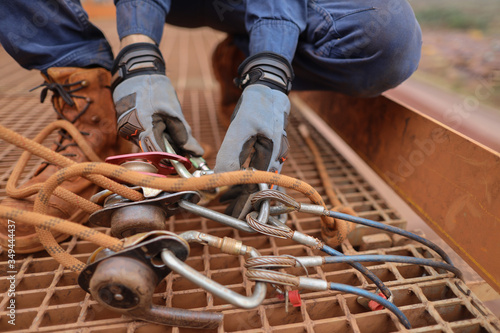 Rope access miner level 3 technician wearing a safety glove conducting safety auditing checking descender, pulley on anchor point prior to work abseiling at construction site, Perth, Australia 