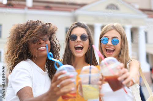 Three trendy cool hipster girls, friends drink cocktail in urban city background.