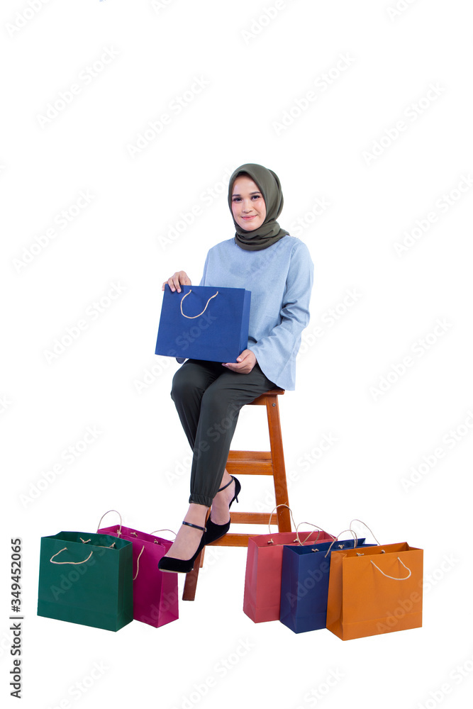 Beautiful women of Muslim Indonesia is holding a shopping bag with a joyful expression sit in chair isolated on white background Beautiful women of Muslim Indonesia is holding a shopping bag with a joyful expression sit in chair isolated on white background