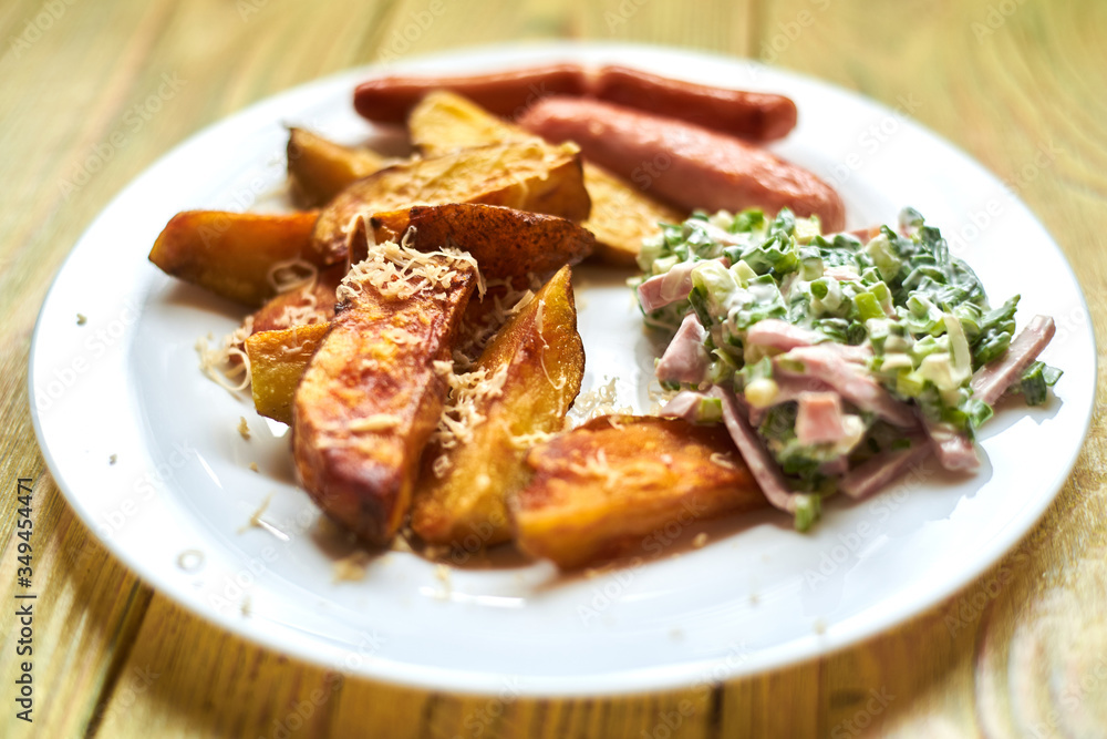 Fried crispy potato with cheese, sausages and salad on a white plate on a wooden background.