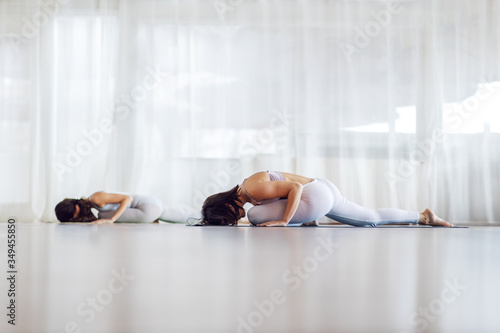 Two attractive fit yogi girls in Sleeping Swan yoga pose. Yoga studio interior.