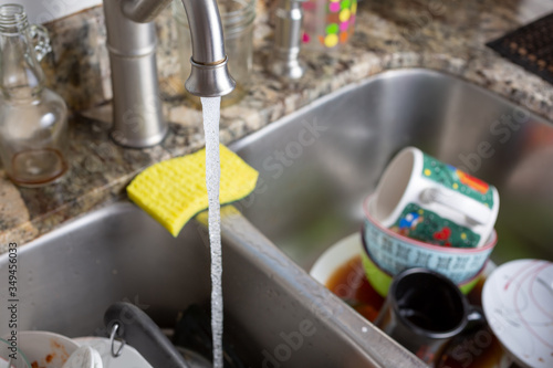 A view of a kitchen faucet fixture with running water and a sink full of dishes.