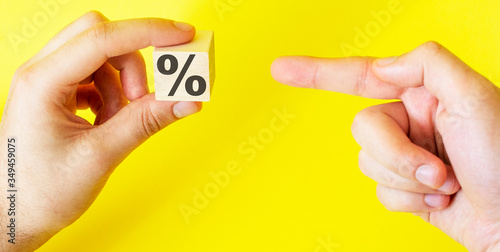 Hand holds a cube on a yellow background with a percent sign