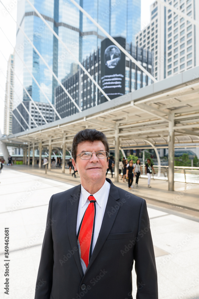 Mature happy businessman in front of modern building at Bangkok city