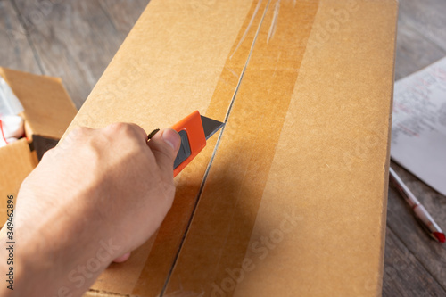 A view of a hand holding a box cutter ready to open a cardboard box shipment package.