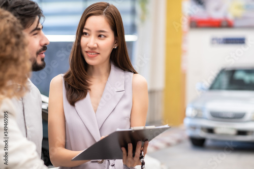 Salesperson working at car dealership.Young Asian woman consultant and couple buyers signing contract for new car in auto show. Concept for car rental or sale.