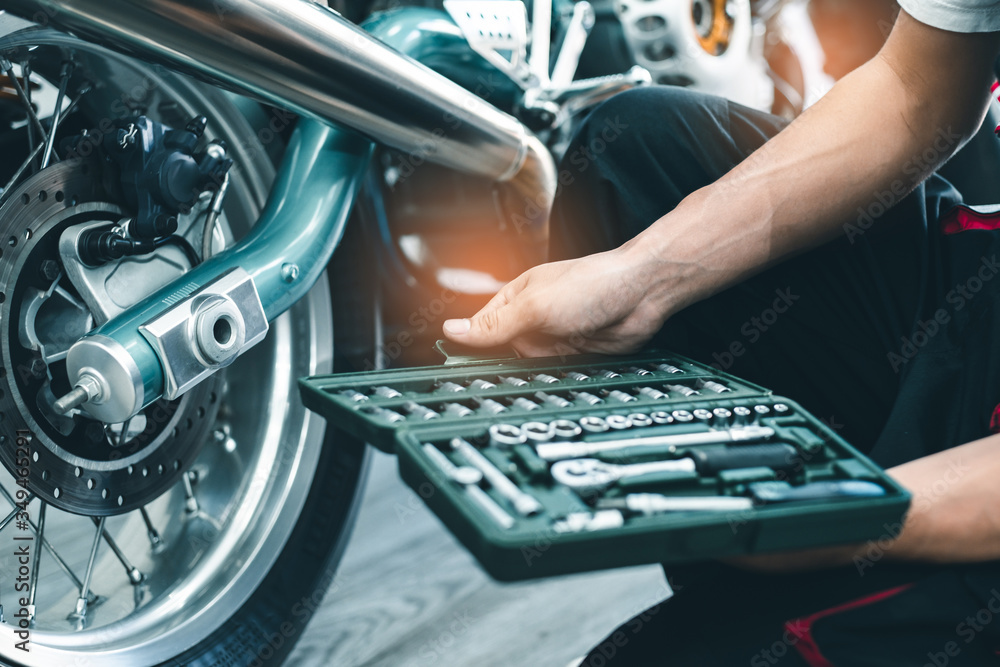 Bike repair. Young man repairing motobike in garage.mechanic fixing  motocycle engine.Serious young man repairing his motorcycle in bike repair  shop. Stock-Foto | Adobe Stock