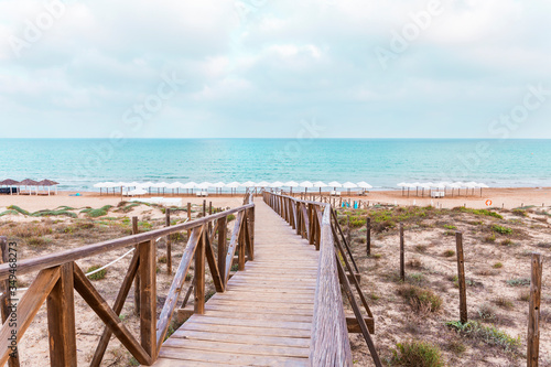 Fototapeta Naklejka Na Ścianę i Meble -  wooden bridge over the protected dunes to access the beach umbrellas in Guardamar. Alicante, Spain