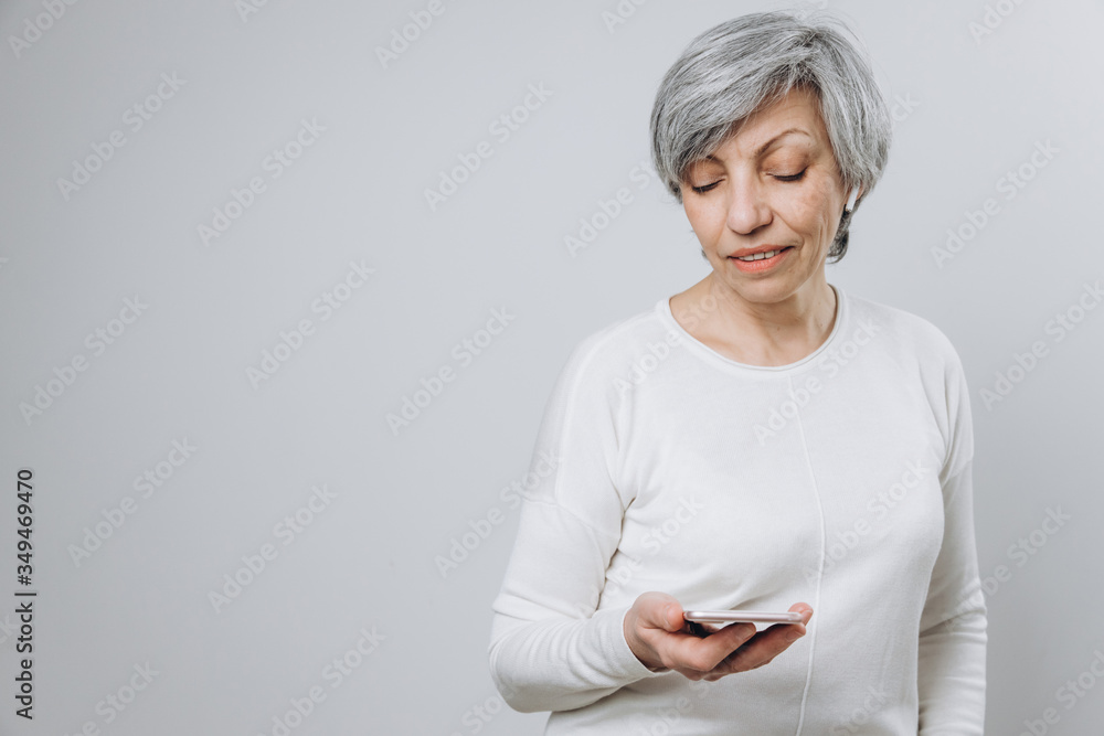 Elderly woman uses a mobile phone with hands free set, against a light background Elderly woman uses a mobile phone with hands free set, against a light background