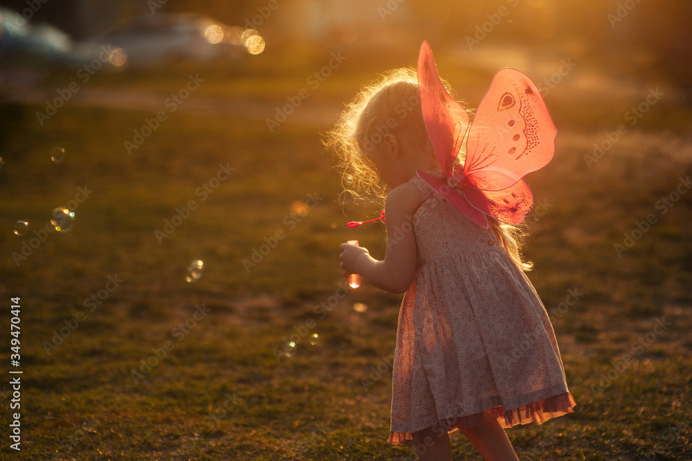 Fototapeta premium little girl plays with soap bubbles in a clearing at sunset at golden hour