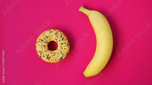Yellow banana and donut on bright pink background. Above view