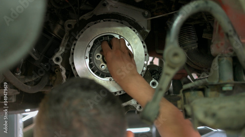 Auto mechanic is installing bolts into metal car clutch. Close up repairman inserting bolts into round car detail. photo