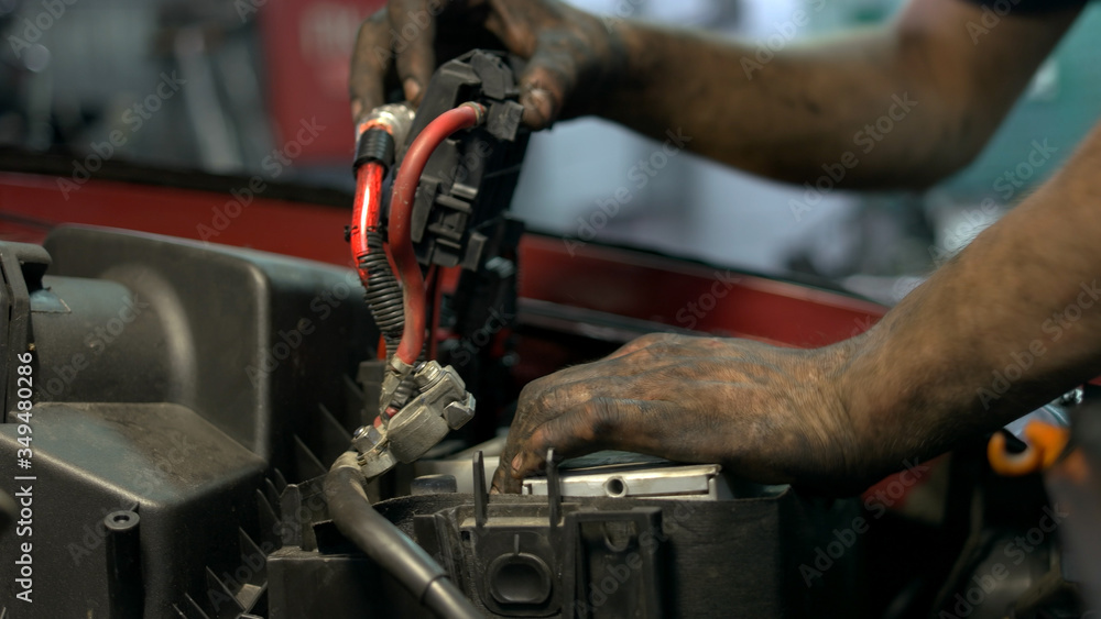 Auto mechanic installing accumulator battery. Dirty hands of repairman.