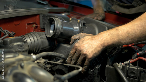 Young professional car service worker installing car engine detail. Repairing fixing car motor.