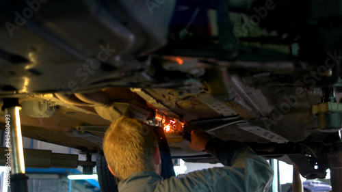 Close-up welding work on a lifted car. View from front side. Mechanic welds the bottom of the car.