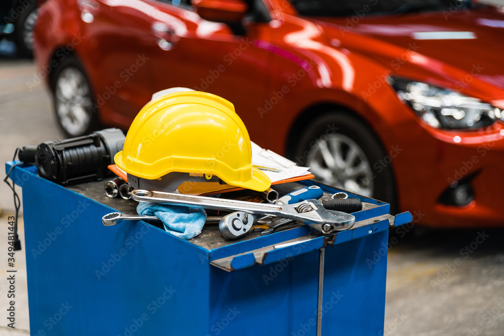 Close-up image of blue metal tool cabinet with safety helmets, glove, document pad on the cabinet with garage background. Automobile repair service.