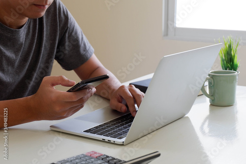 An Asian man uses a laptop at home while sitting at a wooden table. Man hands typing on a notebook keyboard. The concept of young people working at mobile devices.