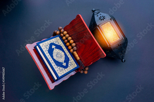 Holy Al Quran with written arabic calligraphy meaning of Al Quran, lantern lamp and rosary beads or tasbih on black background. photo