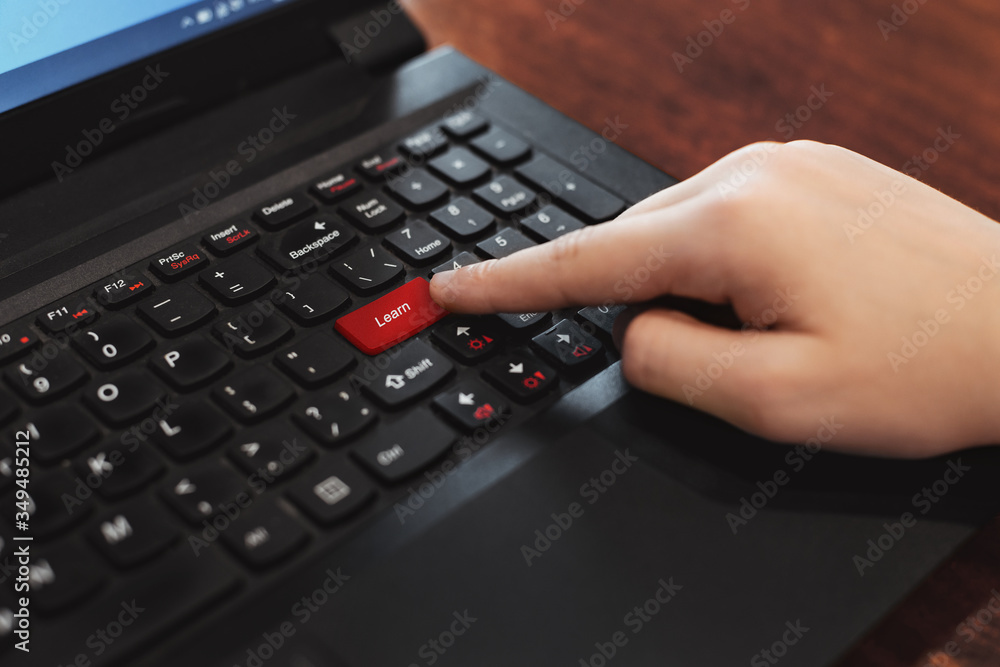 Index finger presses the red button on the black laptop keyboard. Computer keyboard with red key 'Learn' . Distance and e-learning education concept, online lessons Index finger presses the red button on the black laptop keyboard. Computer keyboard with red key 'Learn' . Distance and e-learning education concept, online lessons