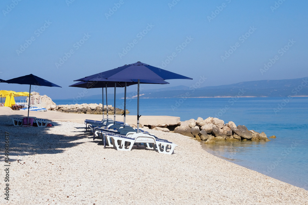 Blue beach umbrellas and chaise for relax and comfort on sea resort. Summer vacations and travel for seaside. Paid service on comfort beaches.