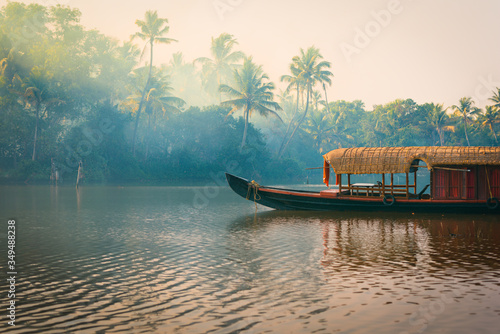 A traditional house boat is anchored on the shores of a fishing lake in the palm tree jungle at sunset, in the Backwaters, a popular destination for yoga retreats and nature lovers in Kerala, India