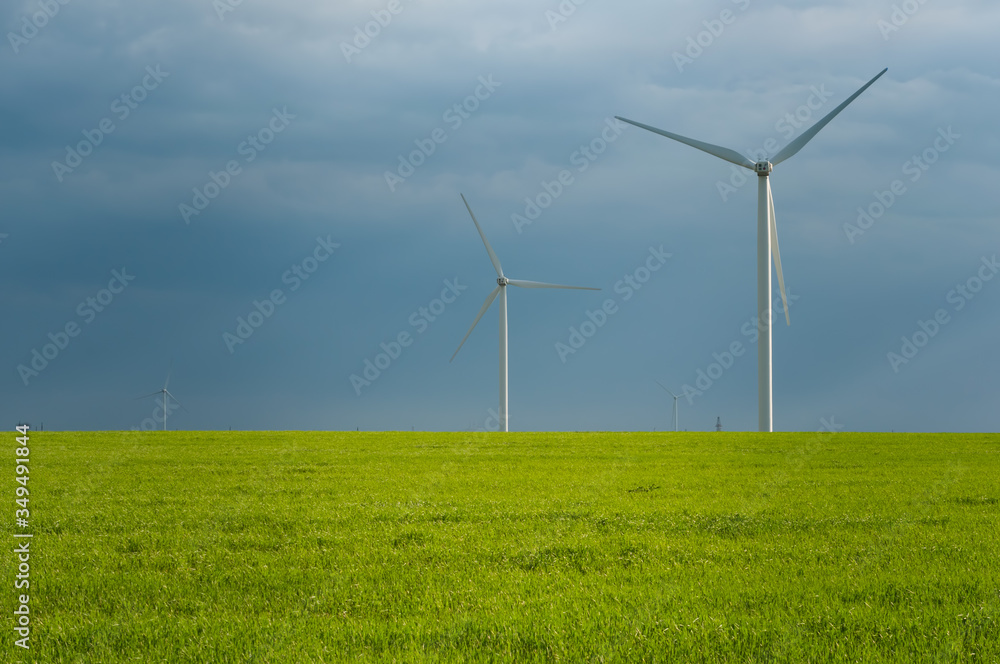 Wind power turbines among green meadow with blue sky in the spring morning. Copy space for text. Green energy concept. Wind power turbines among green meadow with blue sky in the spring morning. Copy space for text. Green energy concept.