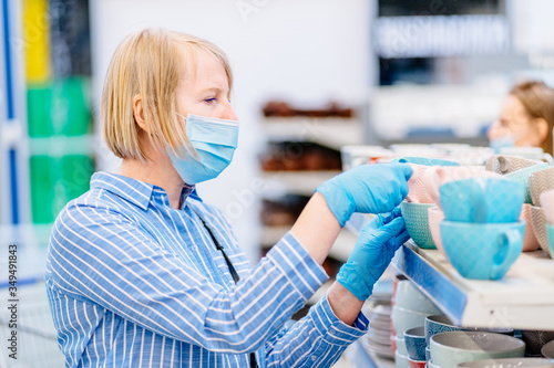 Mature blond female customer in blue shirt looking at a blue mug in a cook shop or supermarket.