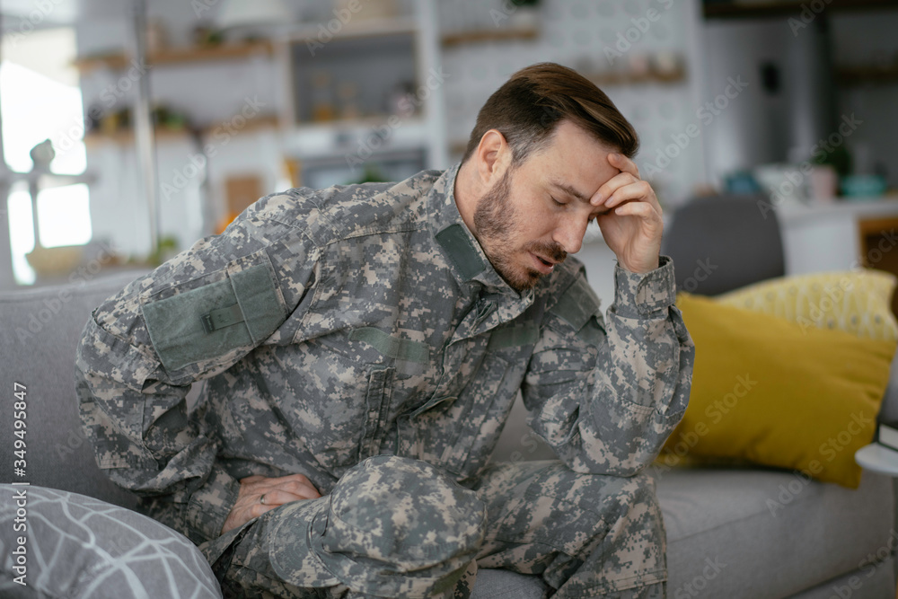 Depressed soldier sitting on sofa in living room. Young marine having PTSD.	