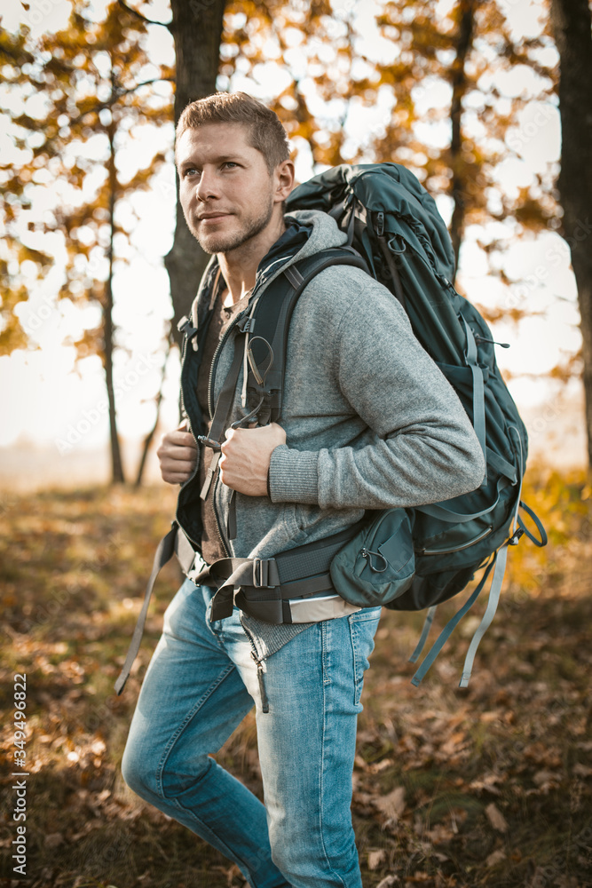 Backpacker travels in nature. Serious Caucasian man with a large backpack looks into the distance while standing against the backdrop of an autumn forest