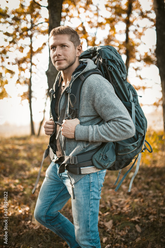 Backpacker travels in nature. Serious Caucasian man with a large backpack looks into the distance while standing against the backdrop of an autumn forest