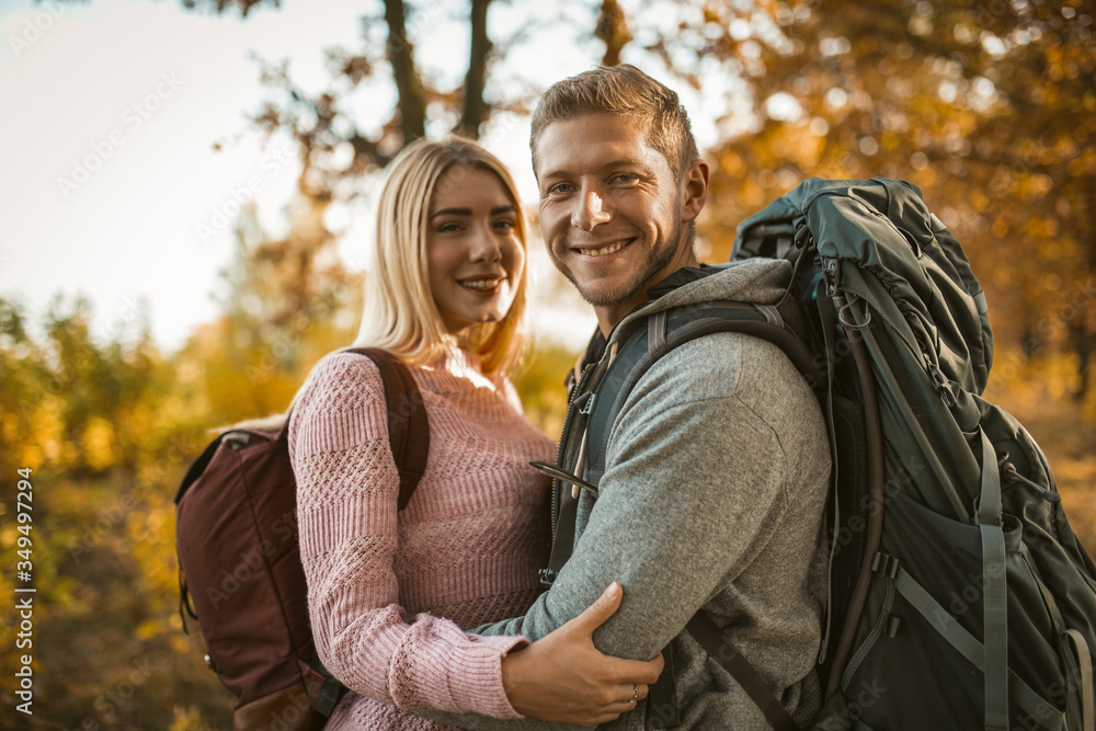 Happy backpackers in love laughs hugging while looking at the camera and standing against the backdrop of autumn nature