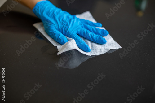 Woman cleaning home office table surface with wet wipes in blue gloves stock photo