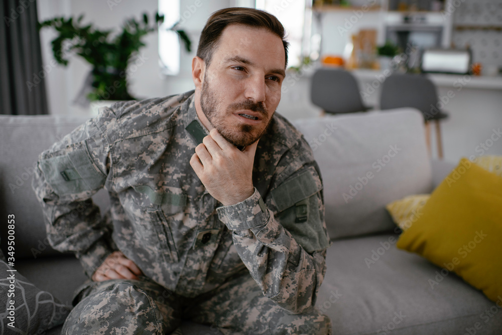 Fototapeta premium Depressed soldier sitting on sofa in living room. Young marine having PTSD. 