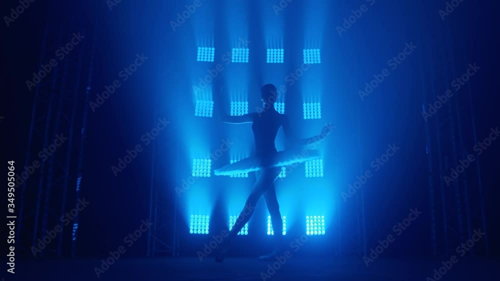 Graceful silhouette ballerina doing a workout in the classroom. Smoke in the rays of blue light. Ballet dancer in white tutu, girl in pointe, whirls around you, slow motion Graceful silhouette ballerina doing a workout in the classroom. Smoke in the rays of blue light. Ballet dancer in white tutu, girl in pointe, whirls around you, slow motion