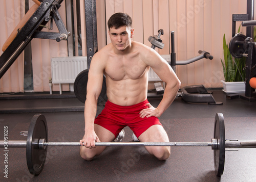 Young man flexing muscles with barbell in gym.