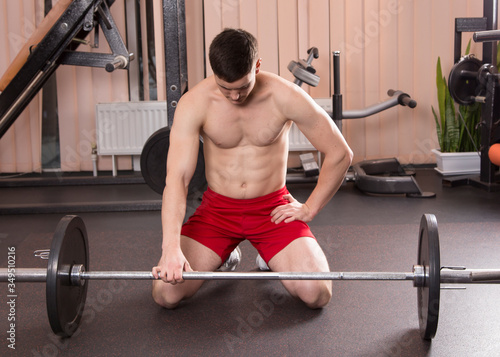 Young man flexing muscles with barbell in gym.