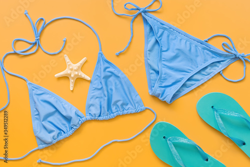 Blue bikini swimsuit  turquoise flip flops and starfish on a yellow background  flat lay. Women s beach accessories. Travel concept. View from above.