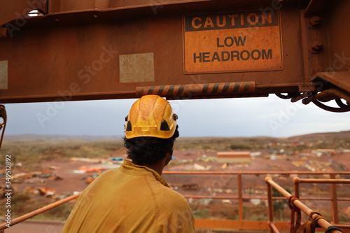 Safety workplace caution sign low headroom attached on beam structure with construction worker wearing a yellow safety hard hat while walking underneath 