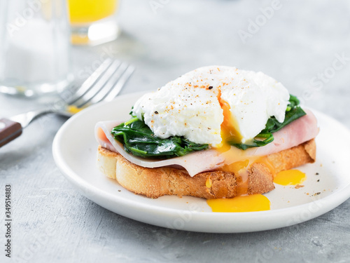 Sandwich with poached egg, spinach and ham with glass of orange juice on background.