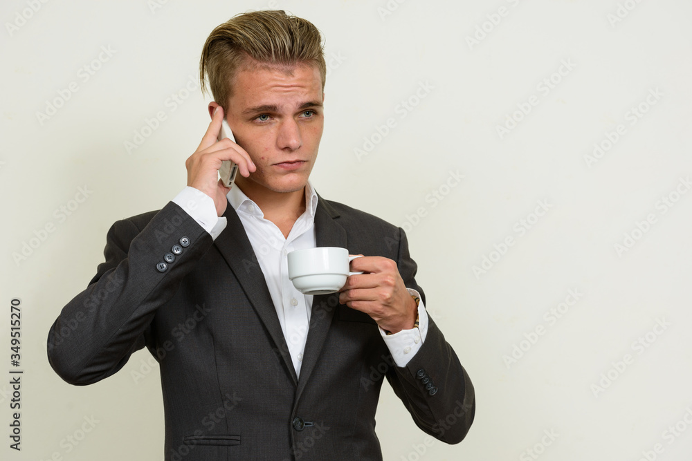 Young handsome blond businessman in suit talking on the phone and drinking coffee Young handsome blond businessman in suit talking on the phone and drinking coffee