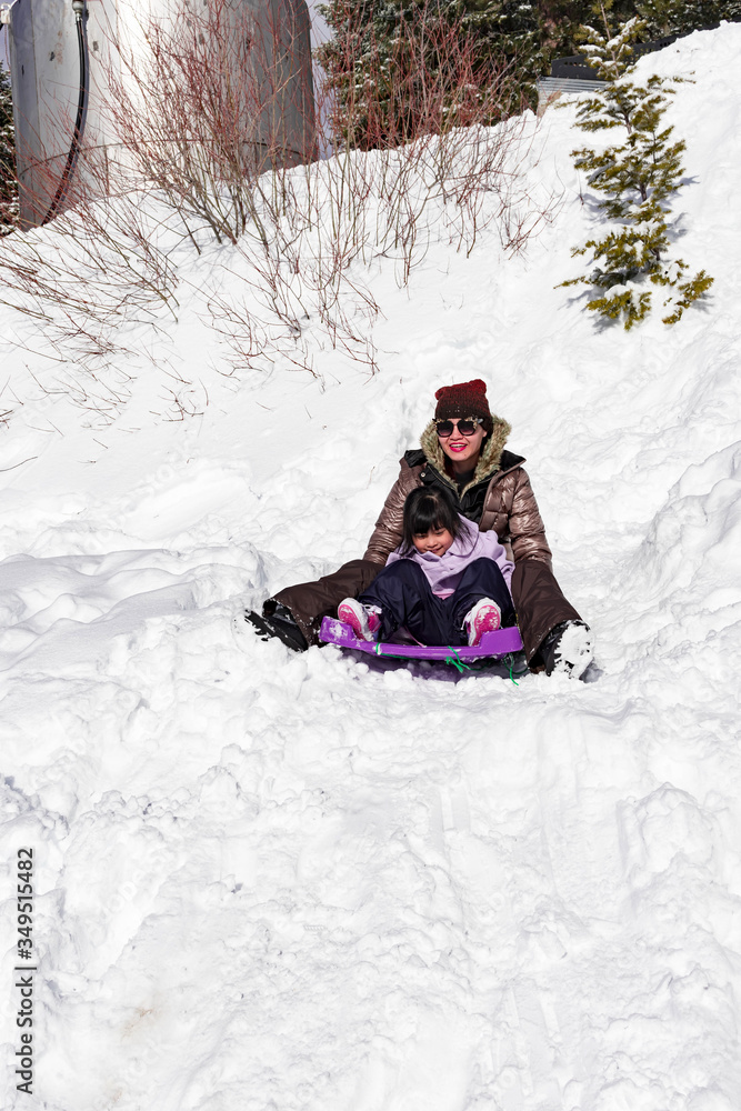 Child while enjoying playing with snow and sliding with mommy