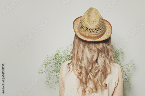 Beautiful blonde woman with curly hair wearing a summer hat, female back