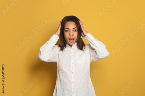 Shocked woman. African American woman opens mouth on vibrant yellow background © millaf