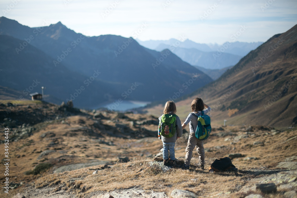 Two children with backpacks in high mountains holding hands looking into the distance