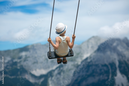 Konstfotografi A boy in a summer hat flies on the swings on a background of rocky mountains