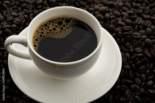 Hot black coffee with foam in a white coffee cup on coffee beans field background